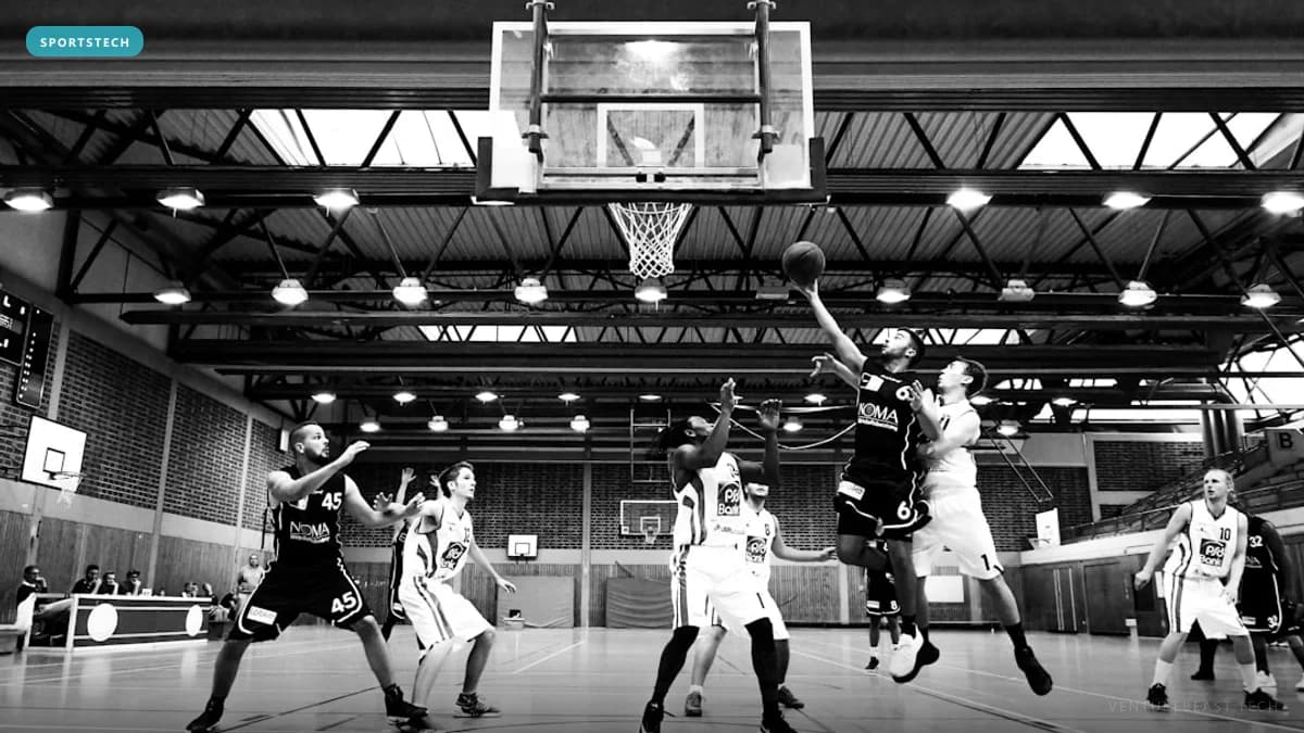 Black-and-white photo of a basketball player leaping for a layup over defenders in an indoor gym