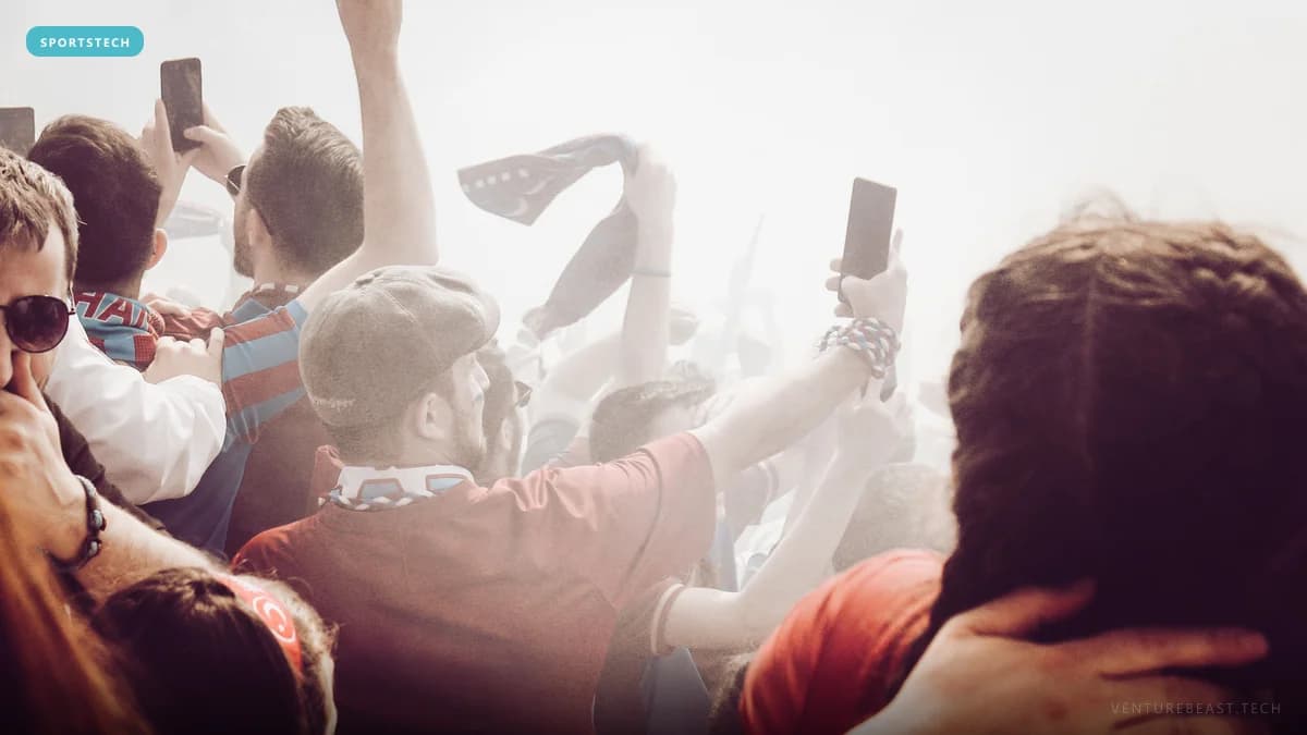 Hazy crowd of sports fans raising phones and scarves in a stadium stand