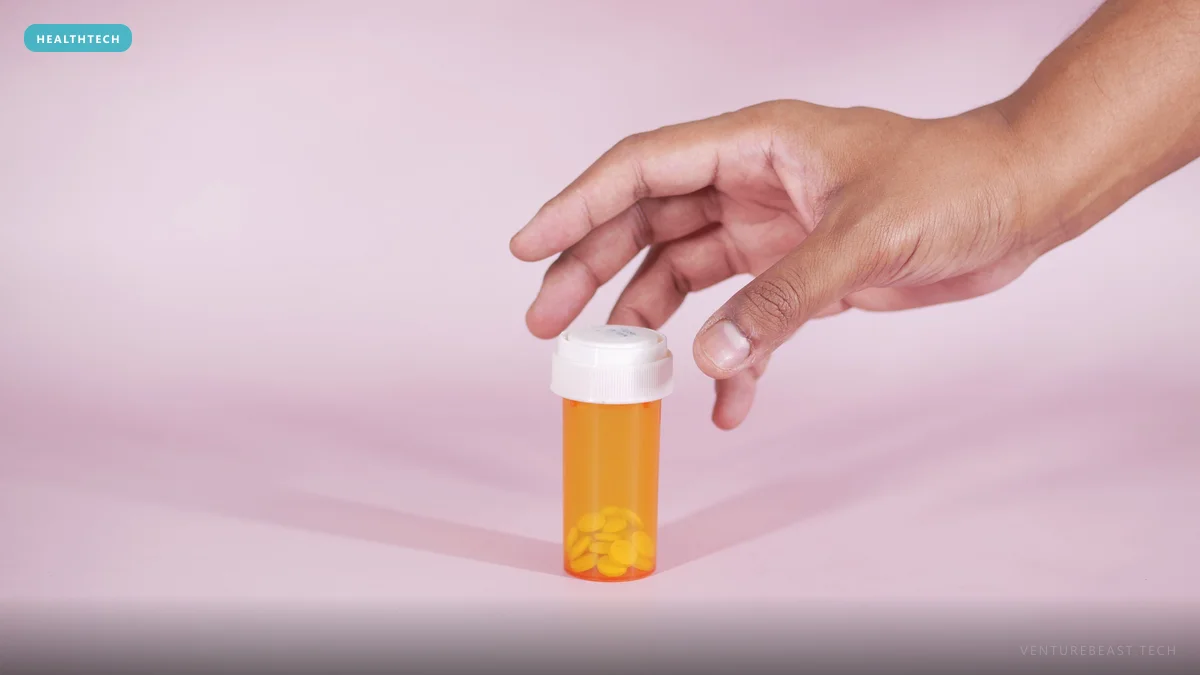 Hand reaching for an orange prescription pill bottle holding a few tablets on a pink background