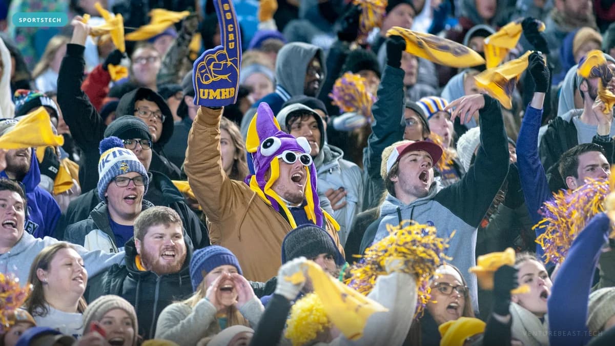 Cheering college sports fans in purple and gold waving yellow towels, one in a purple jester hat and foam finger