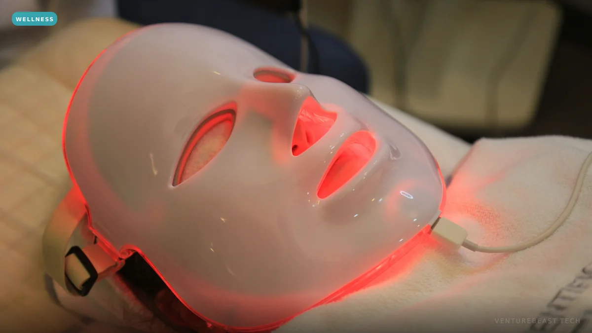 A person lying back wearing a white LED face mask glowing red during a light therapy session