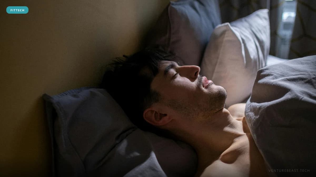 Young man sleeping in bed, head on a gray pillow, lit by soft light from a nearby window