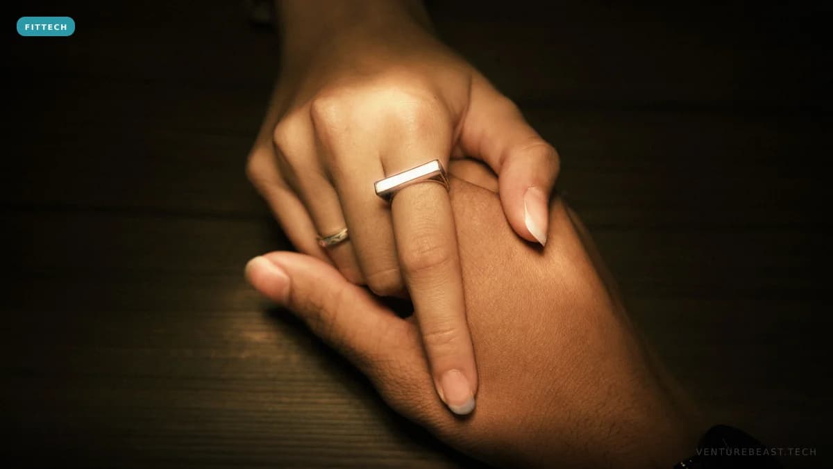 A hand resting on a dark wooden table wearing a slim silver ring on the index finger