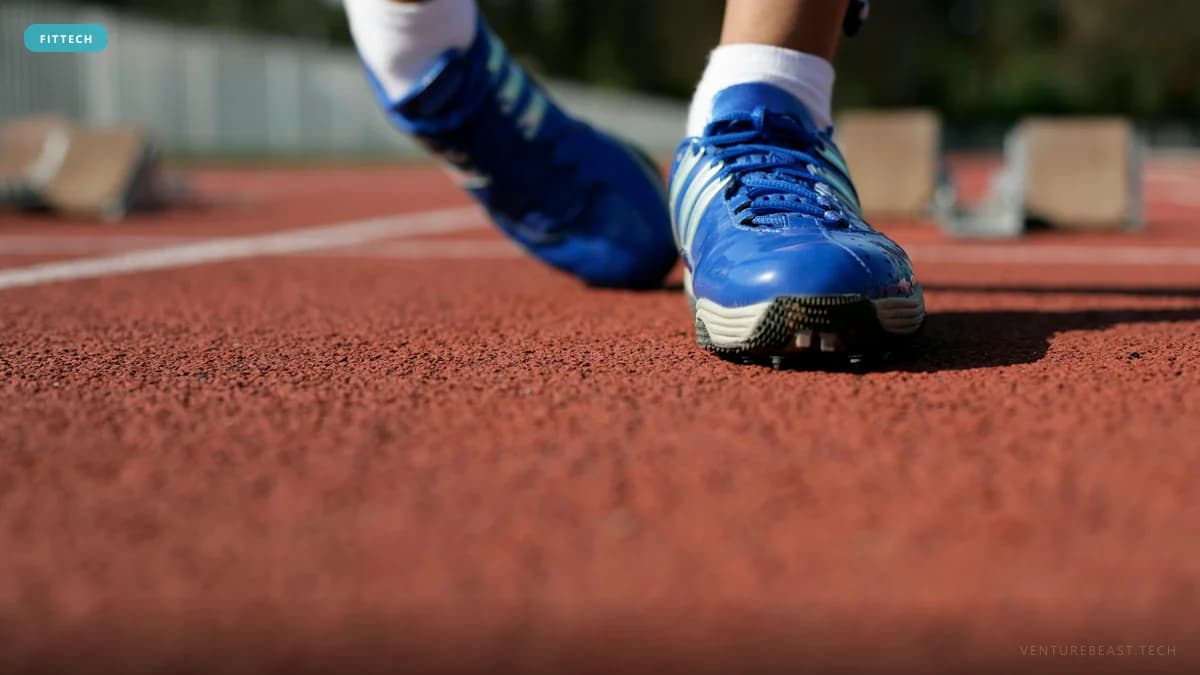 Low-angle close-up of a sprinter's blue spiked track shoes on a red running track near starting blocks