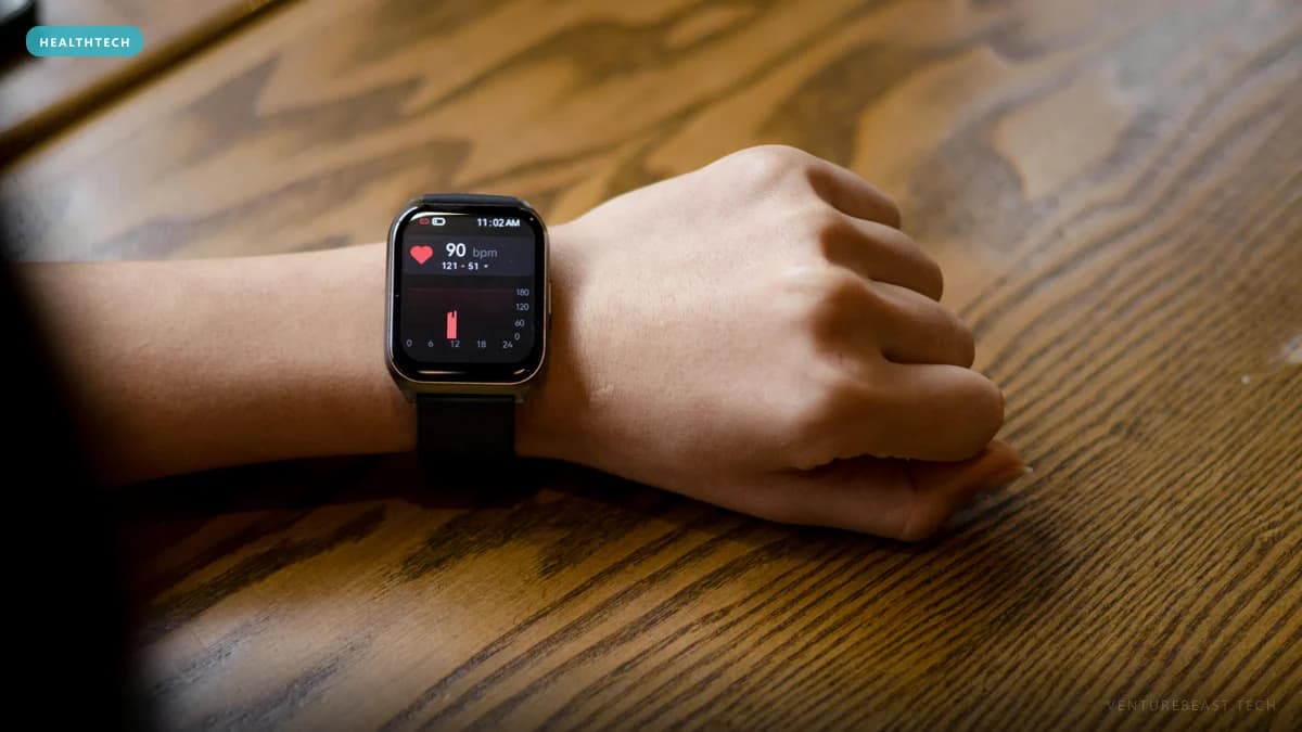 Wrist wearing a square smartwatch that shows a 90 bpm heart-rate reading, resting on a wooden table