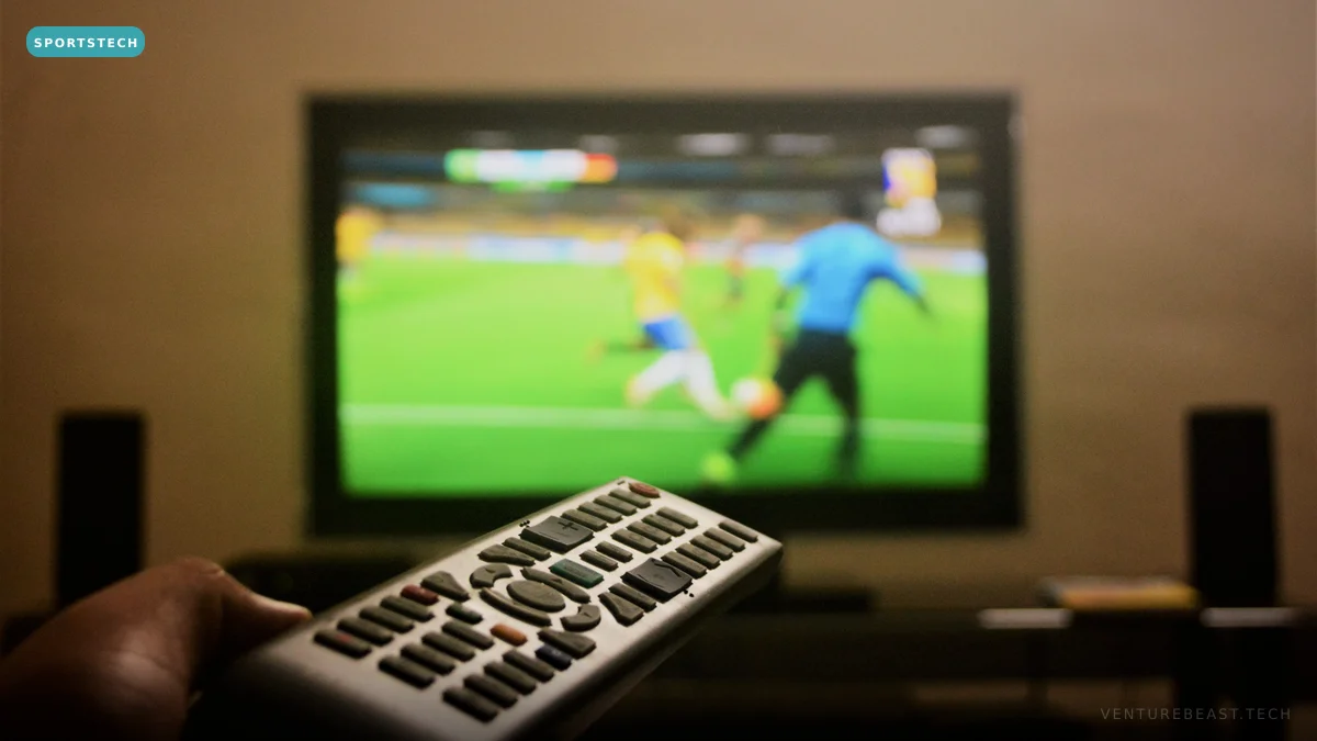 A hand pointing a remote at a TV showing a live soccer match, in a dimly lit living room